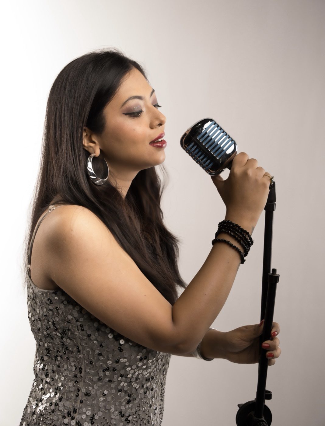 Chaittali Shrivasttava singing into a vintage microphone in a sequined dress